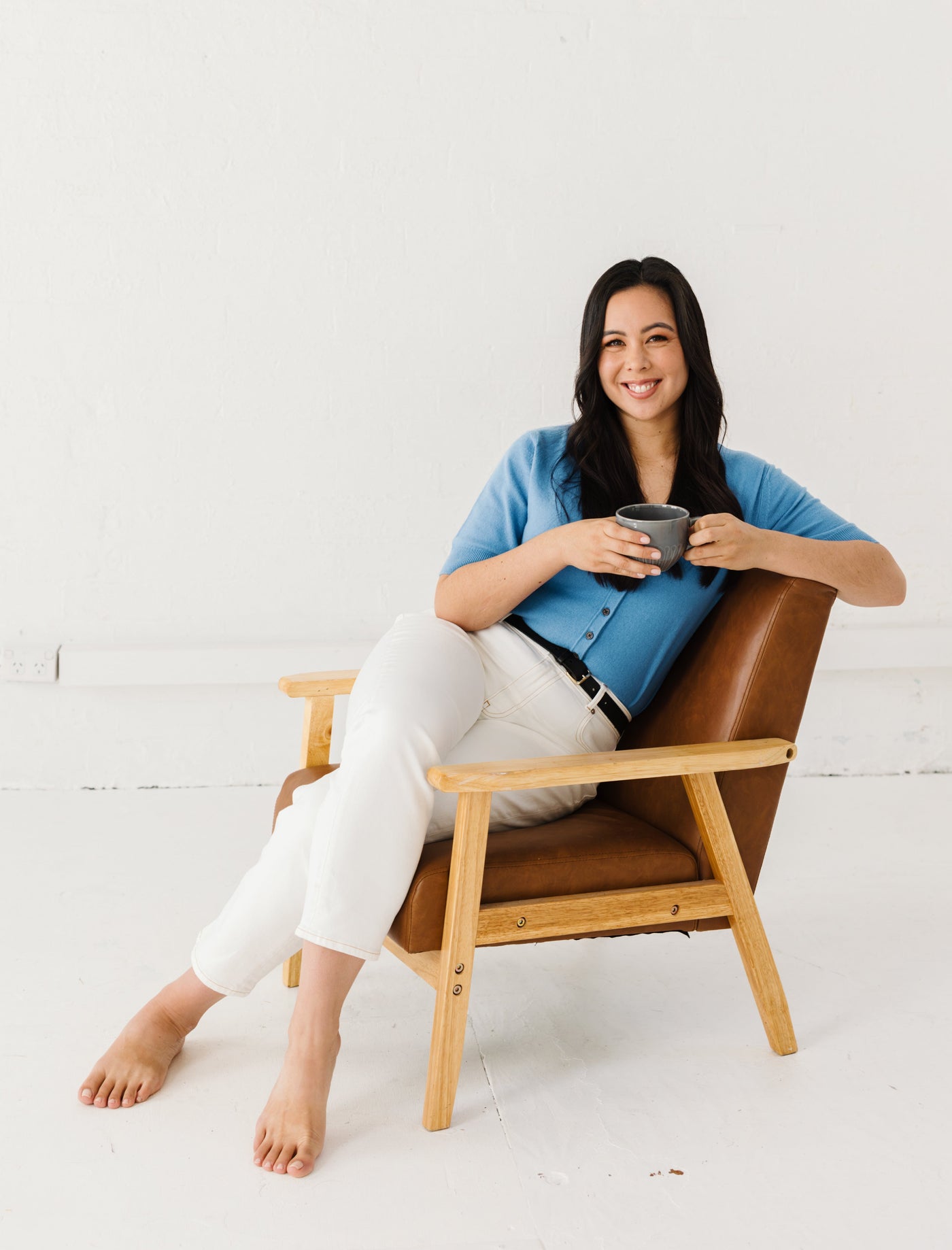 Woman sitting on a brown chair holding a mug against a white background